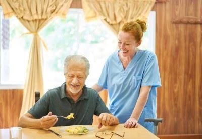 nurse standing with patient while the patient uses aids to help eat